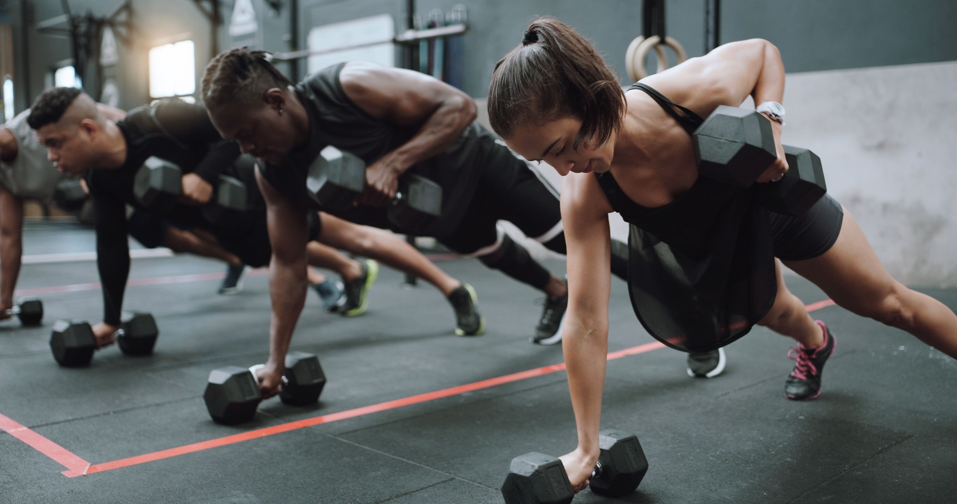 Shot of a group of sporty young people doing pushups and renegade rows together in a gym